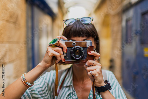 An attractive tourist with a camera. A beautiful woman with a camera takes pictures of beautiful places. The girl raises the camera to her face and takes a photo.