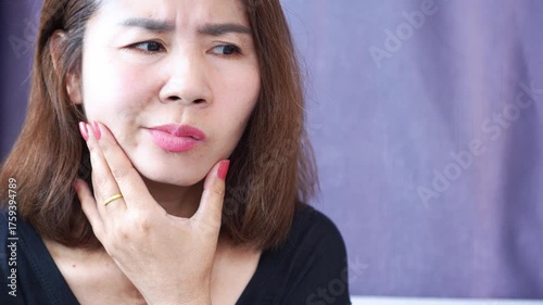 Asian woman with Bell’s palsy or facial paralysis, holding her face and checking and shows facial weakness and a drooping mouth, possibly caused by viral infection, nerve damage, or stress.  medical, 