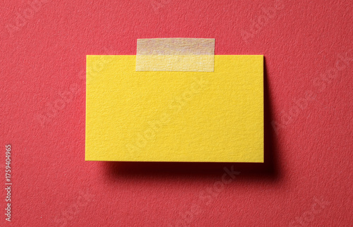 Obraz na płótnie Yellow blank paper note with adhesive sticky tape and shadow on red background