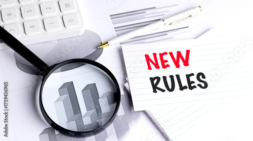New rules message on notecard with magnifying glass, pen, calculator and business charts in office setting