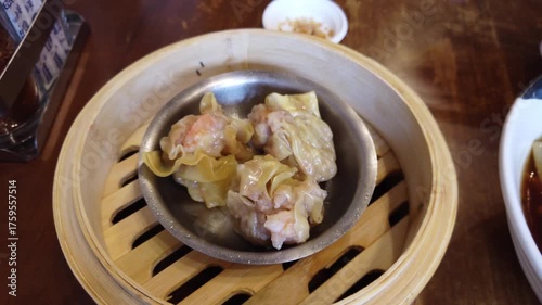 Close-up of delicious steamed shrimp and pork dumplings served in a small metal dish inside a bamboo steamer basket. Traditional Chinese dim sum dish popular in Asian cuisine and local restaurants.