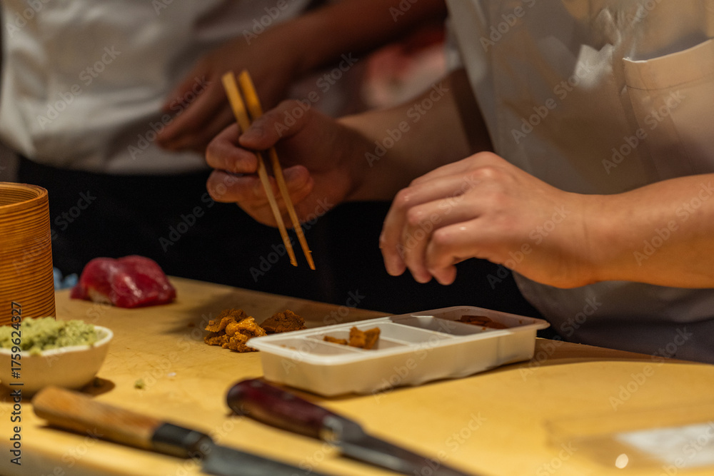 Obraz premium Skilled chef preparing sushi with chopsticks in a vibrant kitchen setting