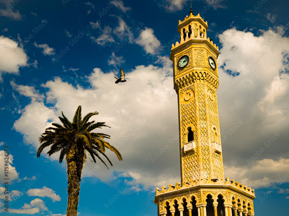 Fototapeta premium Scenic view of Izmir Clock Tower with a palm tree and a bird in flight under a clear sky. A symbolic landmark in Turkey’s Aegean region, reflecting urban and coastal harmony.