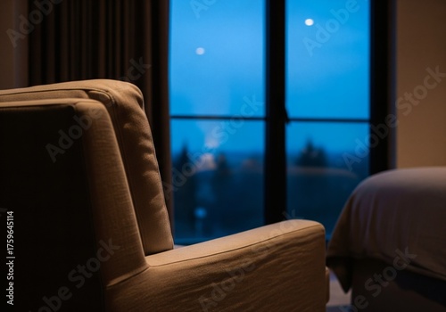 Close-up of a cozy armchair in a dark room looking out a window at a deep blue twilight sky