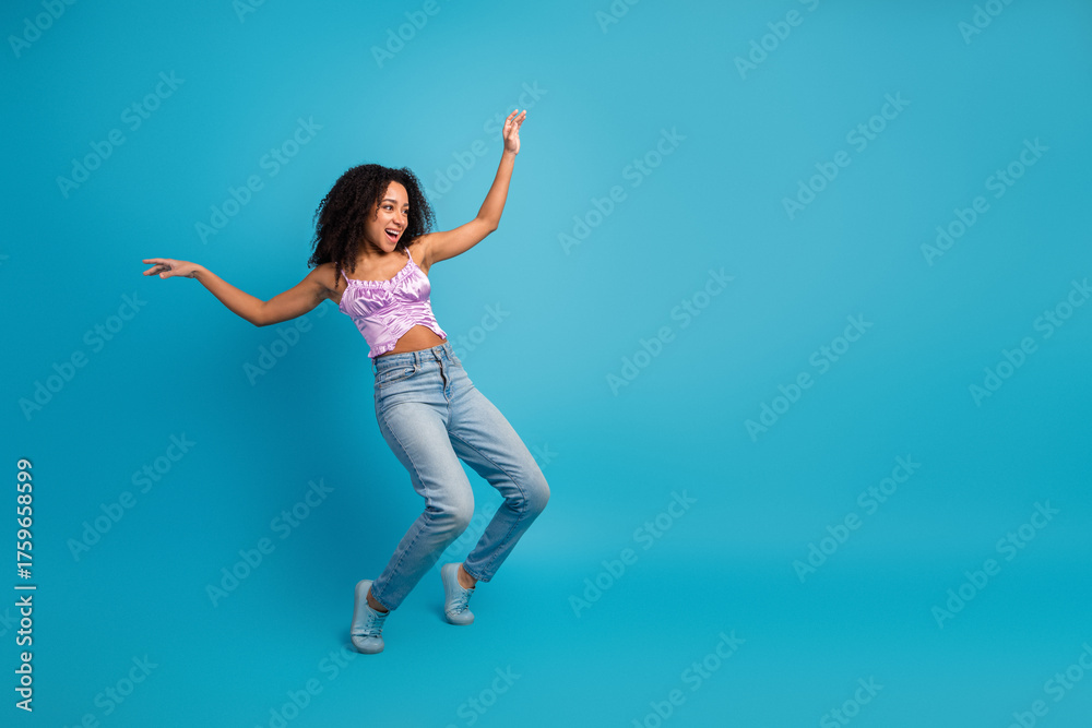 Obraz premium Young girl dancer in pink top and jeans jumps against blue background expressing joy energy and carefree lifestyle