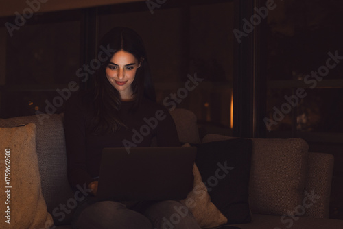 Photography Close up of one young happy cheerful woman smiling and using laptop computer at home sitting on sofa working and studying alone at late night