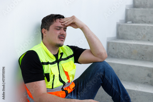 Construction worker in safety vest sitting on stairway with hands on head, showing signs of stress, fatigue, or headache. Concept of burnout, job pressure, mental health, and labor exhaustion.
