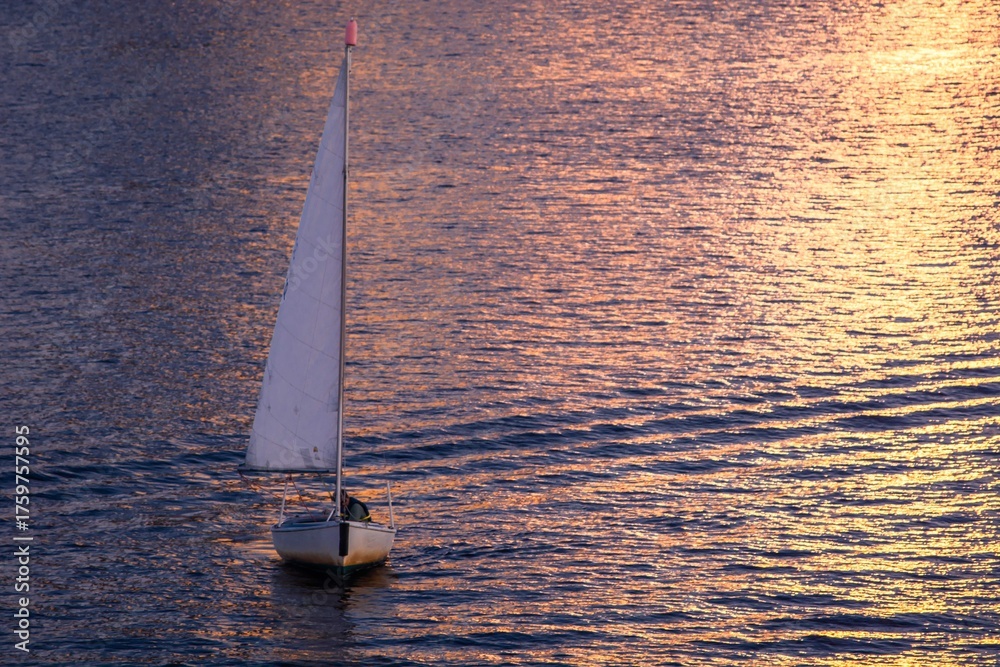 Ταπετσαρία Sailing into the Sunset: A lone sailboat glides effortlessly across the shimmering water under a sky painted with the golden hues of the setting sun, evoking a sense of serene freedom and adventure
