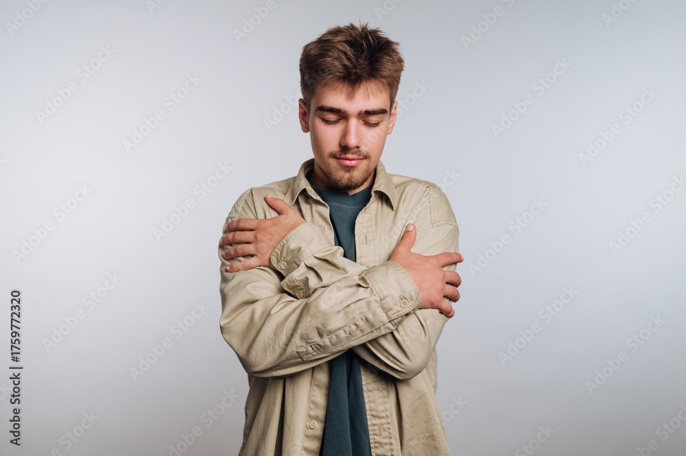 Fototapeta premium Young man expressing self-embrace and contemplation in a studio setting during daylight hours