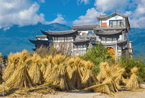 Landanwesen in China nähe Ohrensee. Im Vordergrund angehäufte Stengel von der Reisernte. Bauernof in typiscen Baustil. Landwirtschaft, Ernte, Reis, Haus.