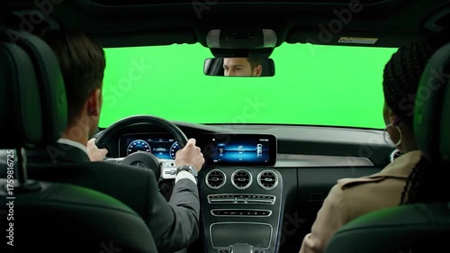 Two people driving a car with a green screen in front of them.