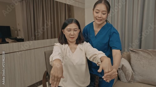 asian female caregiver assisting senior woman with physical therapy exercise at home during rehabilitation process to improve mobility strength and overall health care support in daily life