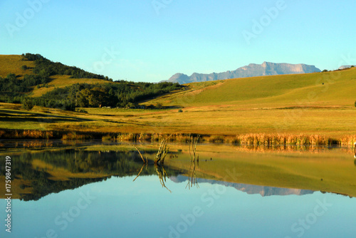 Beautiful landscape photo of a dam on an early misty morning, trees, mountains in the background, and reflections in the blue water.