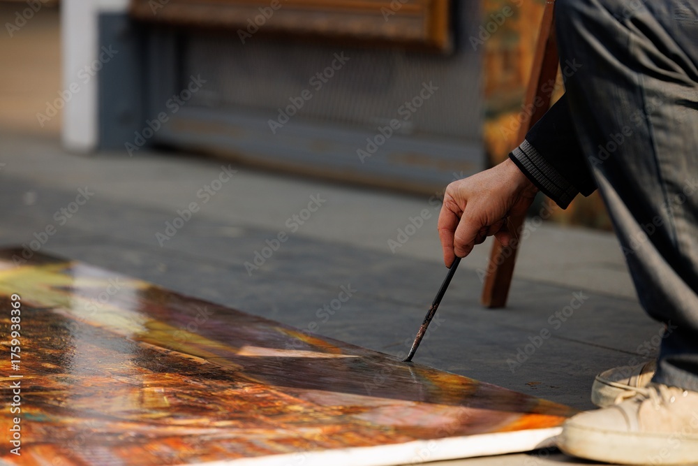 Obraz premium A talented individual is passionately painting on the ground, surrounded by the warm glow of autumn sunlight.
