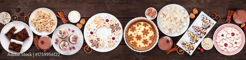Christmas holiday cookies and desserts table scene. Top view on a dark wood banner background. Eggnog pie, an assortment of cookies, fruit cake, cupcakes and chocolate eggnog.