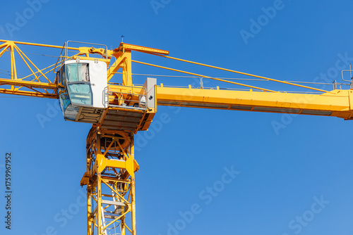 A yellow construction crane towers over a building site on a sunny day with bright blue skies above.
