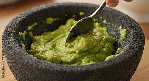 Fototapeta Naklejka Na Ścianę i Meble -  A spoon mashing avocado inside a molcajete in a rustic setting with natural shadows and warm tones.