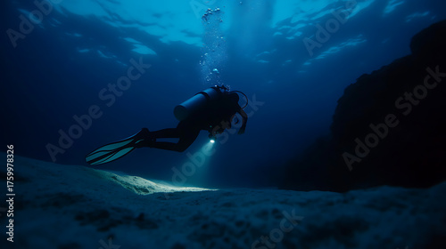 A diver explores the underwater world, the light cuts through the darkness. Bubbles rise as they glide over the sea floor, surrounded by deep blue.