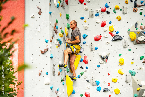 Athletic Man Climbing Indoor Rock Wall: Focused Climber Scaling Colorful Artificial Holds In Modern Climbing Gym With Strong Light And Dynamic Angles