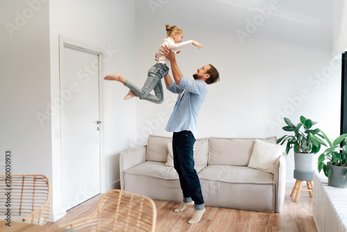 Father joyfully tosses daughter in the air, symbolizing energy, freedom, and the playfulness essential to a balanced lifestyle in tech-integrated home life.