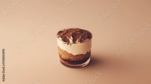 Single-serving tiramisu in a glass cup placed on a warm beige background