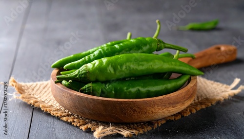 Fresh green chilies in a wooden bowl on a rustic surface