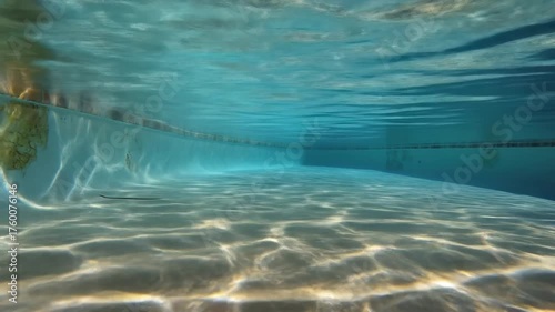Mesmerizing underwater view of a clear blue swimming pool with vibrant sunlight ripples dancing on the tranquil bottom.