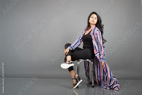 A female dancer sits on a metal stool, striking a lively, expressive pose as her striped long coat swirls around her. Perfect for fashion, lifestyle, empowerment, and creative movement concepts.
