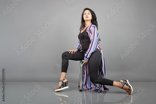 A female dancer sits on a metal stool, striking a lively, expressive pose as her striped long coat swirls around her. Perfect for fashion, lifestyle, empowerment, and creative movement concepts.