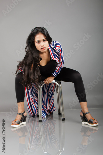 A female dancer sits on a metal stool, striking a lively, expressive pose as her striped long coat swirls around her. Perfect for fashion, lifestyle, empowerment, and creative movement concepts.