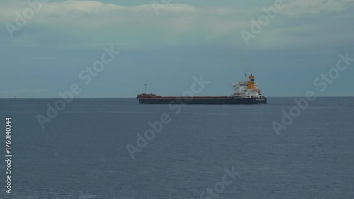 A bulk cargo carrier ship travels on a calm sea, cloudy sky