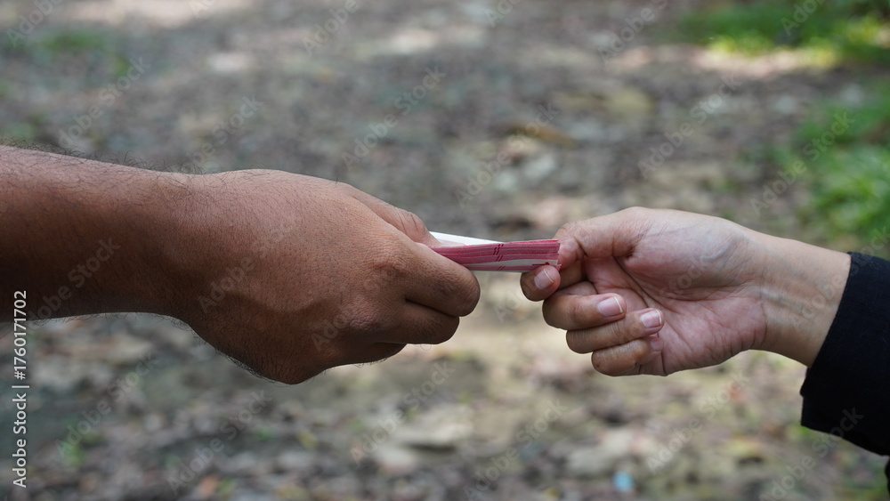 Αυτοκόλλητο A close-up of one hand giving a money to another hand against a blurred outdoor background