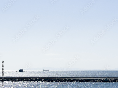 A submarine on the surface of the ocean with sparkling seas and a lighthouse in the foreground