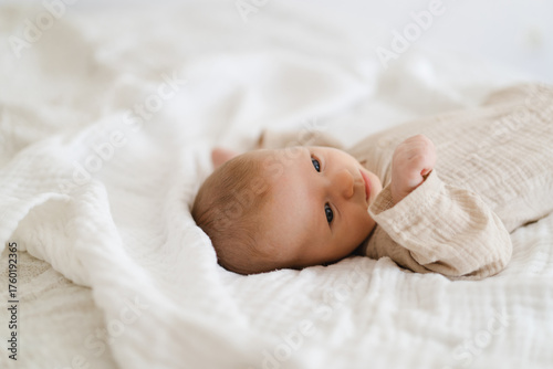 Cute baby lying on a soft white blanket with a calm expression while raising arms. Beautiful portrait of a child. Newborn baby lying on bed