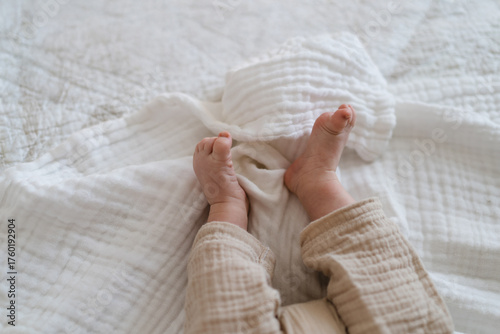 Tiny baby feet peek out from a soft, light-colored blanket on a cozy bed. The peaceful, warm indoor setting creates a serene atmosphere for the sleeping child.