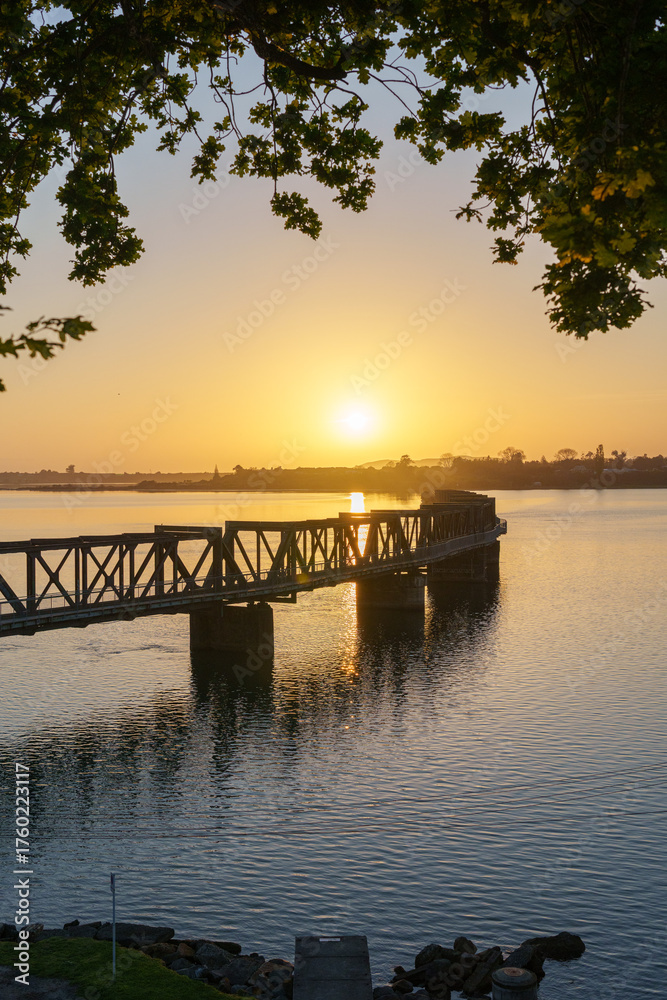 Obraz premium Sun rises over Tauranga harbour and historic railway bridge on calm morning
