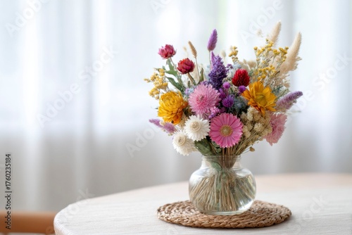 a bouquet of dried flowers, including strawflowers and gerbera daisies, is arranged in an elegant display on the table.