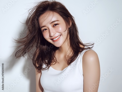 白い背景で髪をなびかせて笑顔を見せる白い服の若い女性ポートレート写真