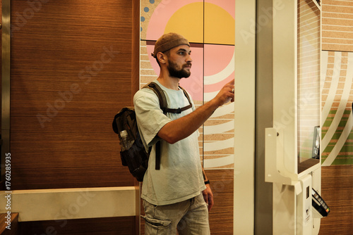 Young man using a digital self-service kiosk to place an order in fast food restaurant. Concept of technology, modern lifestyle, and convenience