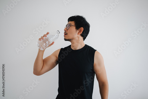 A fit athletic man is enjoying a refreshing drink of water in a sleek minimalist setting isolated over white background.