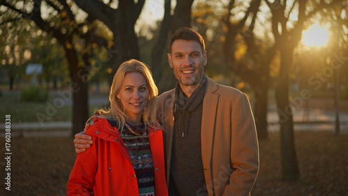 Happy couple smiling at the camera in a park during the autumn season