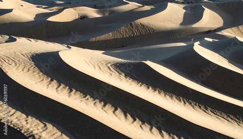 Fototapeta Naklejka Na Ścianę i Meble -  Wavy pattern of sand dunes under warm sunlight, creating shadow play