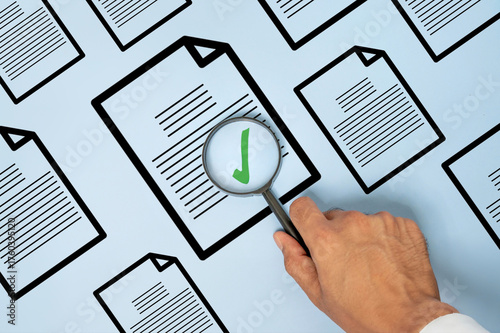 Hand holding a magnifying glass over a document with a green check mark. Document verification, quality control, audit, approval, compliance, and inspection concept.