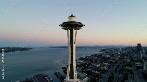 Elevated perspective showcases a tall structure dominating the cityscape, positioned against a serene, colorful sunset sky, with expansive water and distant structures in the horizon during the...