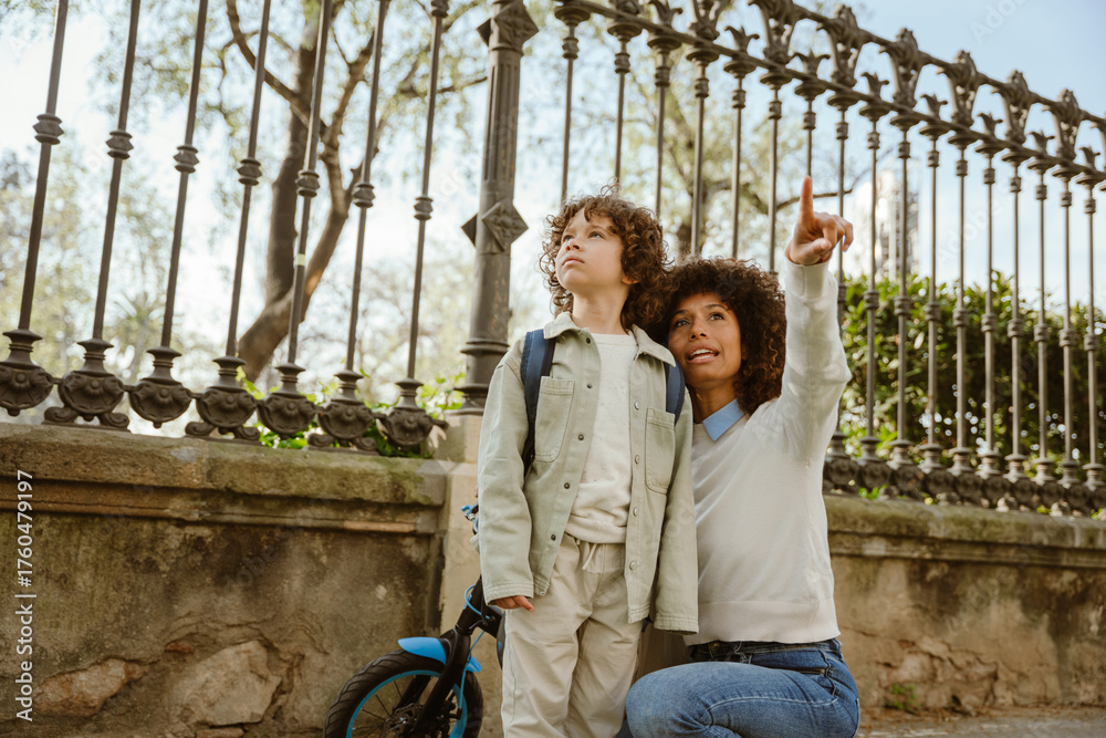 Obraz premium The mother points to the side and sits while talking to her son who is standing next to her by the bicycle