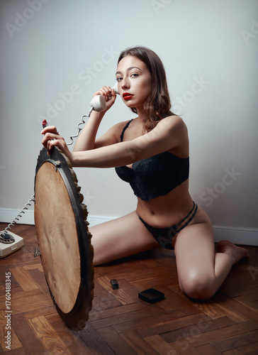 Portrait of lovely girl in black lingerie. Beautiful young woman sitting on floor at mirror with red lipstick and handset (phone)