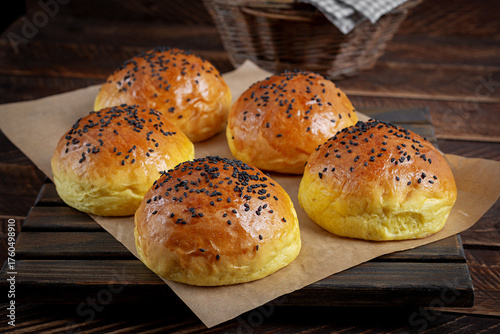 Homemade freshly baked plain golden brown soft hamburger buns topped with sesame seeds against wooden background. Homebaking, freshness, bbq concept