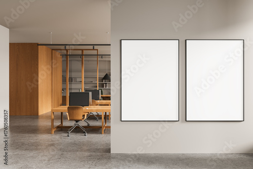 Modern office interior with blank white posters on partition wall and wooden desks in background illuminated by ceiling lights. 3D Rendering