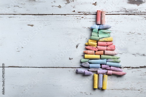 An overhead shot of colorful art pastels arranged to form a Christmas tree shape on a distressed white and gray wooden background.