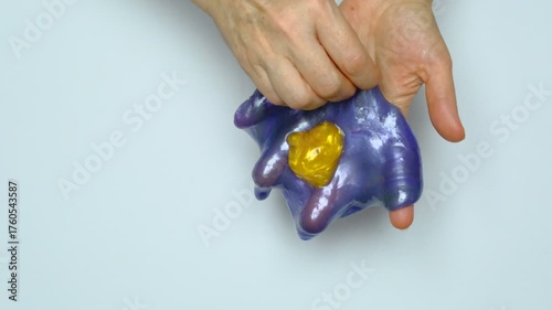 Human hands squeeze a viscous colorful slime. View from above. On a white background. Relaxation, calming down. 